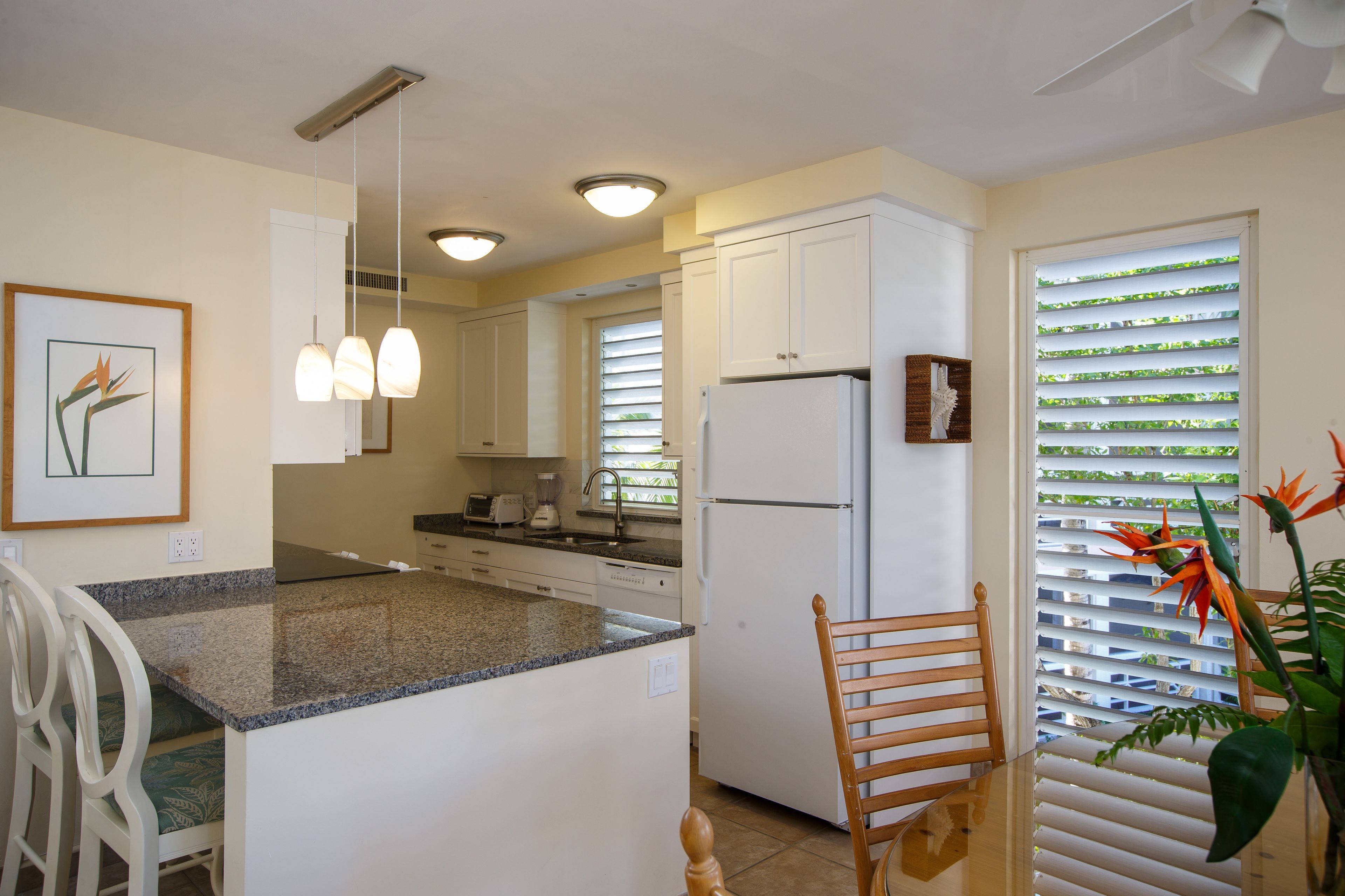 A kitchen with white cabinets, a granite countertop, a white refrigerator, and a dining area with a wooden chair.