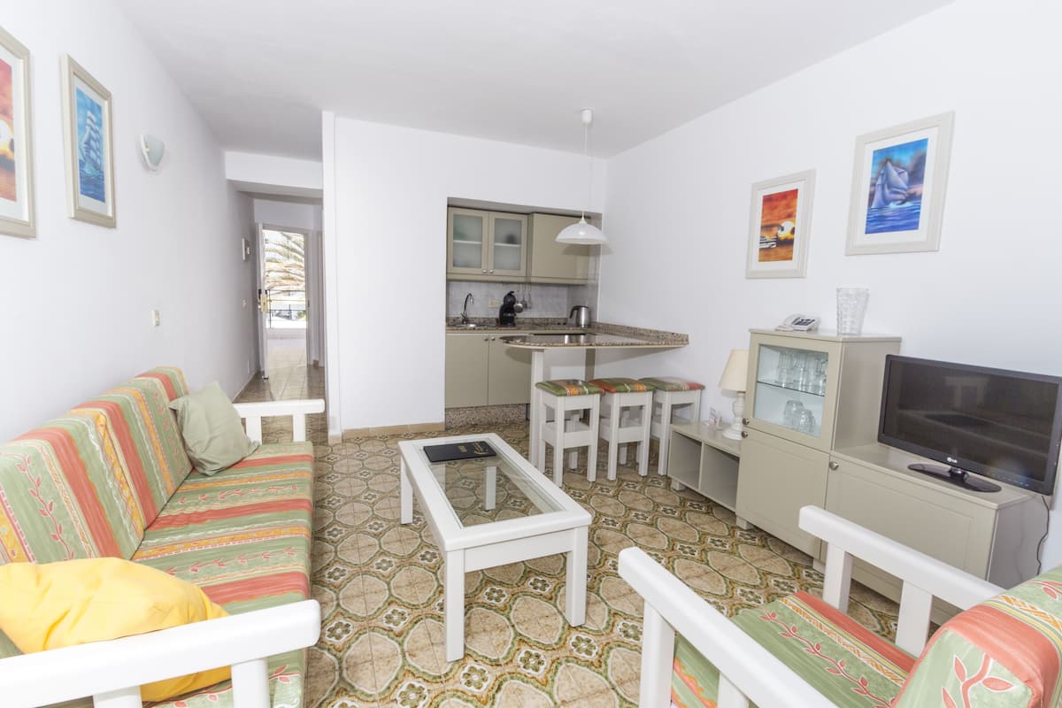 Un espace de vie compact comprenant un canapé, une table basse, un téléviseur et un petit coin cuisine.