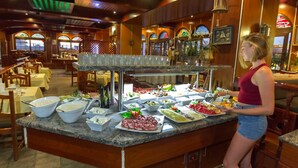 A buffet setup with various food items and a woman serving. - Apartments Maritim Playa - Adults Only (San Bartolomé de Tirajana)
