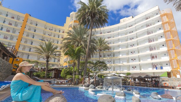 A hotel pool area with a large pool, palm trees, and a multi-story building in the background. - Apartments Maritim Playa - Adults Only (San Bartolomé de Tirajana)