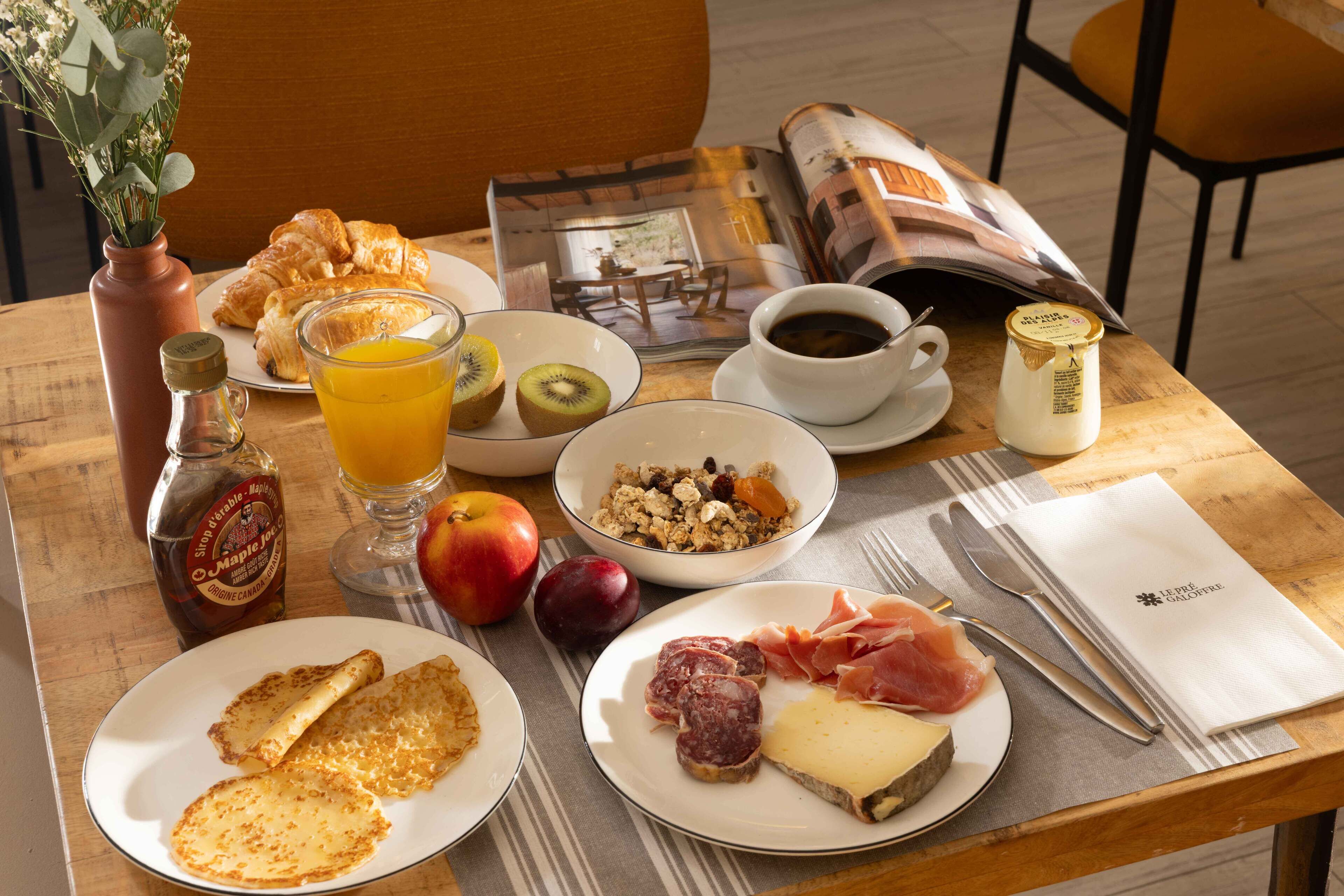 A breakfast table with croissants, fruit, cheese, ham, and a newspaper.