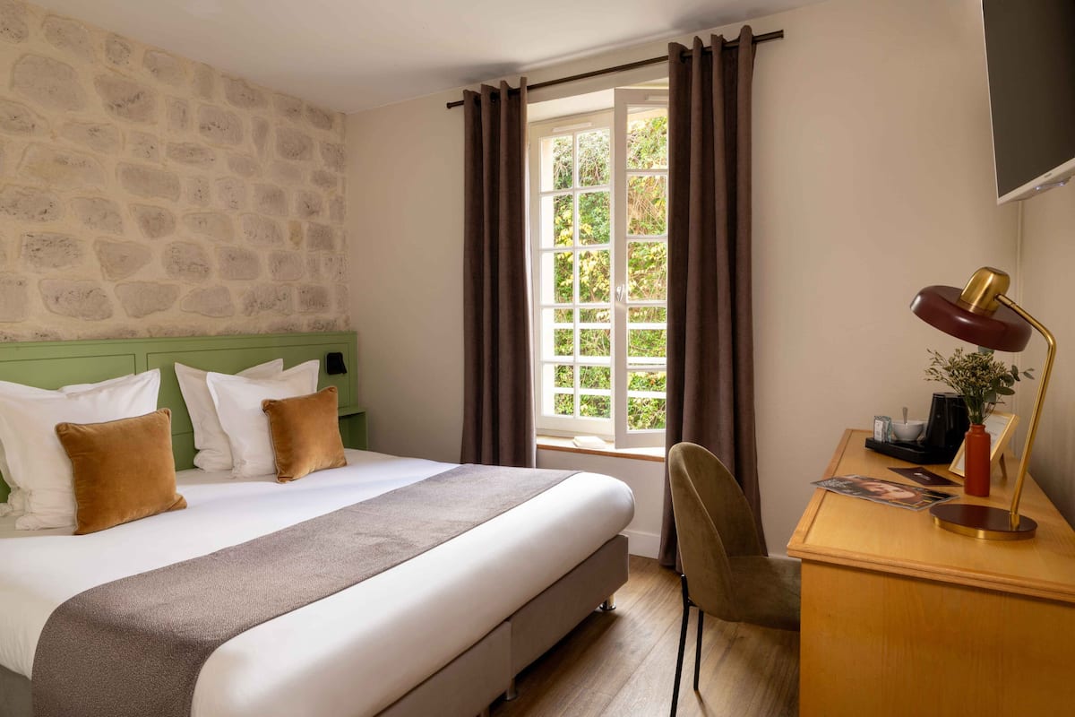 Ein Hotelzimmer mit einem großen Bett, einem Schreibtisch mit Lampe und einem fenster mit Vorhängen.