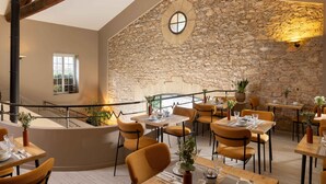 A restaurant with stone walls, wooden beams, and orange chairs. Tables are set with plates, glasses, and cutlery.