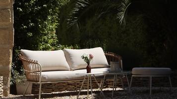 A beige sofa with cushions, a wicker chair, a small round table, and a potted plant with flowers.