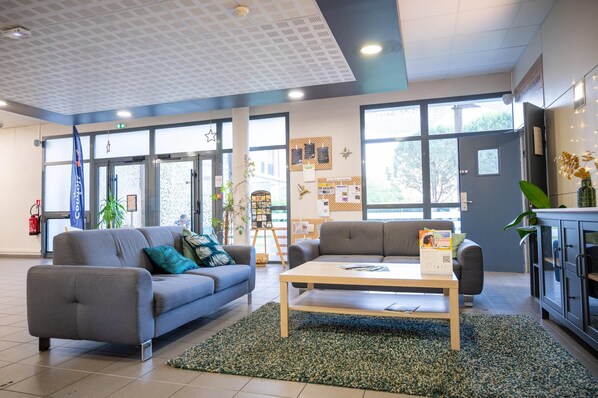 A modern lobby with two grey sofas, a wooden coffee table, and a green rug.