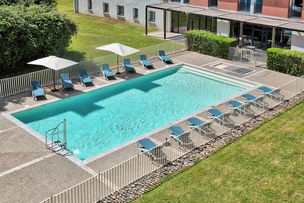 A rectangular swimming pool with a metal deck, surrounded by a white fence, and equipped with lounge chairs and umbrellas. - Comfort Aparthotel Toulouse Metropole (Toulouse)