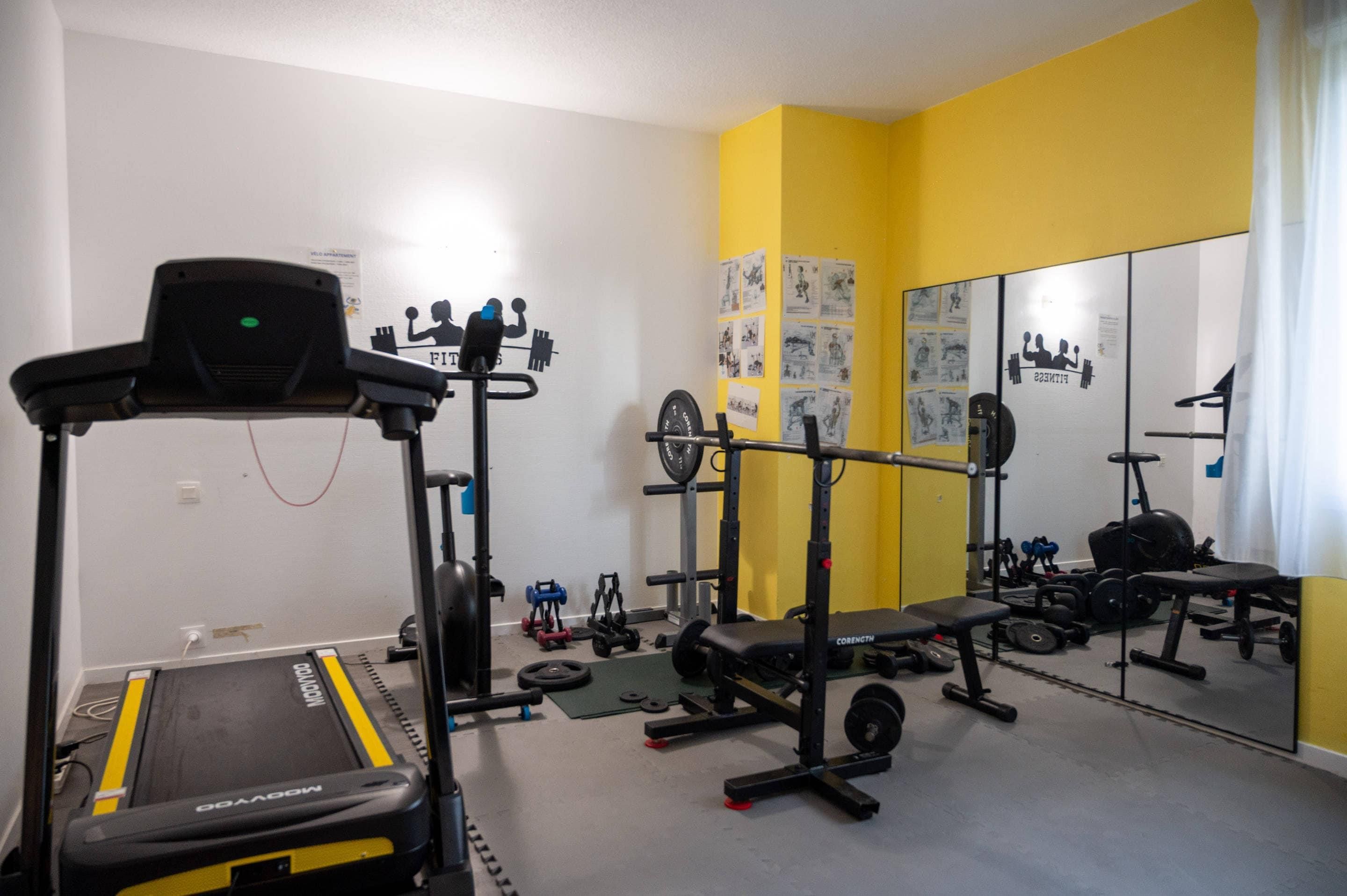 A gym with a treadmill, weight bench, squat rack, and various weights.