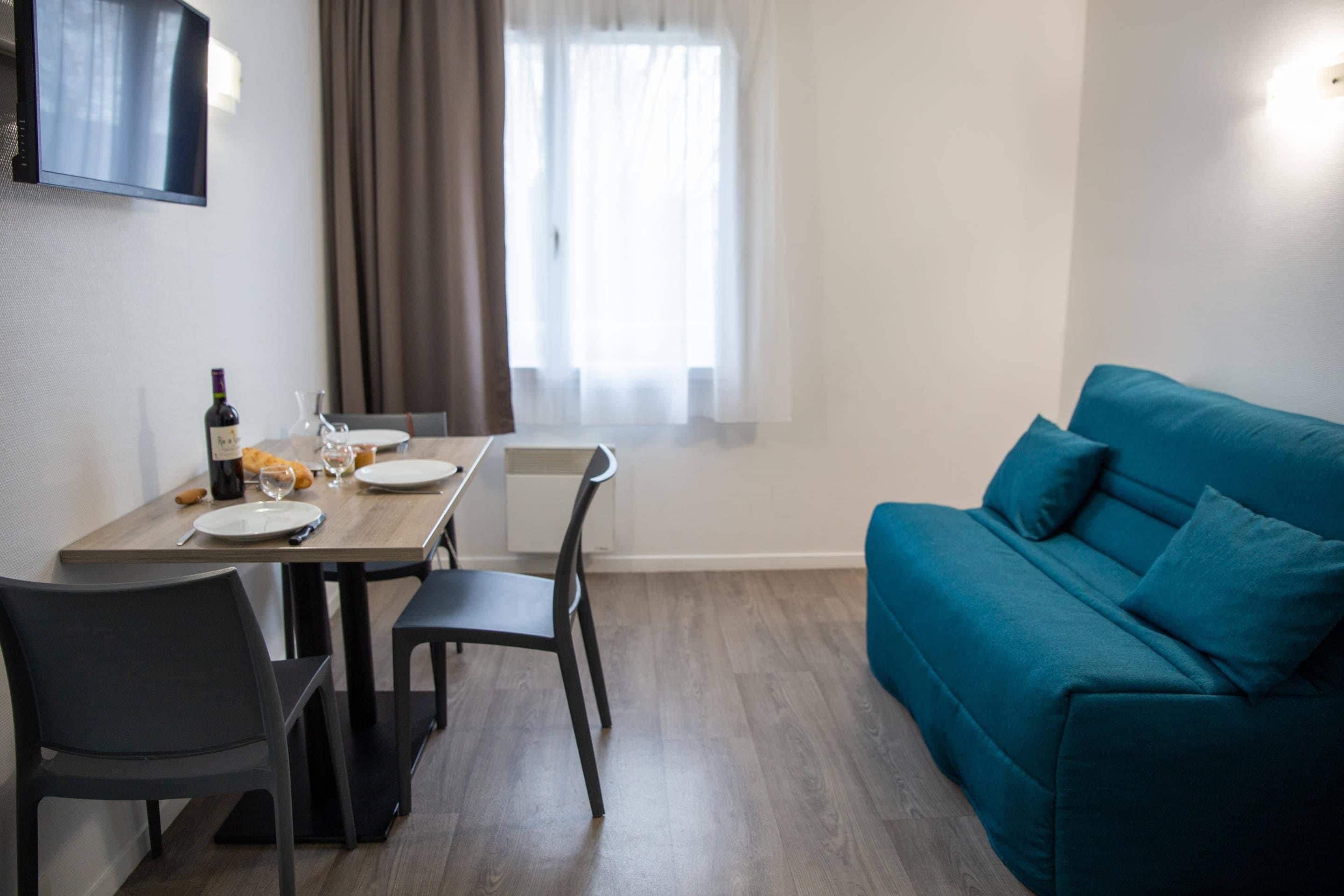 Un soggiorno moderno con tavolo da pranzo, sedie, un divano blu e una TV a parete.