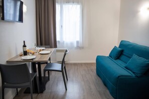 A modern living space with a dining table, chairs, a blue sofa, and a TV mounted on the wall. - Comfort Aparthotel Toulouse Metropole (Toulouse)