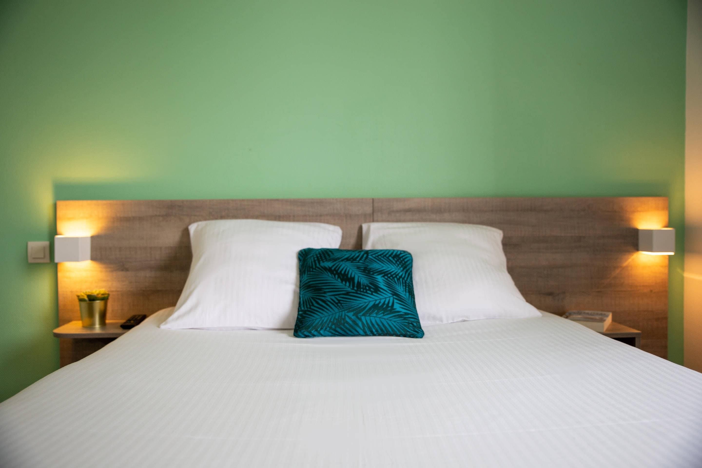 A bed with white linens, a teal pillow, and two bedside lamps.