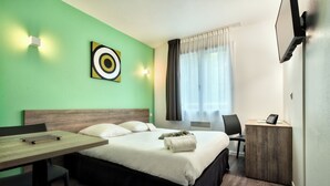 A hotel room with a bed, a desk, a chair, a TV, and a window with curtains. - Comfort Aparthotel Toulouse Metropole (Toulouse)