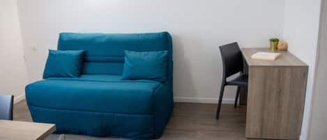 Ein Zimmer mit einem türkisblauen Sofa, einem Holztisch und einem Sessel.