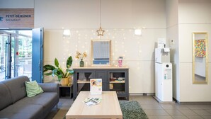 A modern breakfast area with a sign for Petit Déjeuner, a refrigerator, a coffee machine, a small table with brochures, a sofa, and a potted plant. - Comfort Aparthotel Toulouse Metropole (Toulouse)