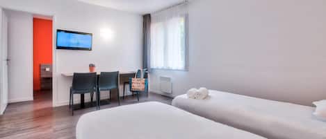 Une chambre d’hôtel avec deux lits, un bureau avec une chaise, un téléviseur fixé au mur et une fenêtre avec des rideaux.