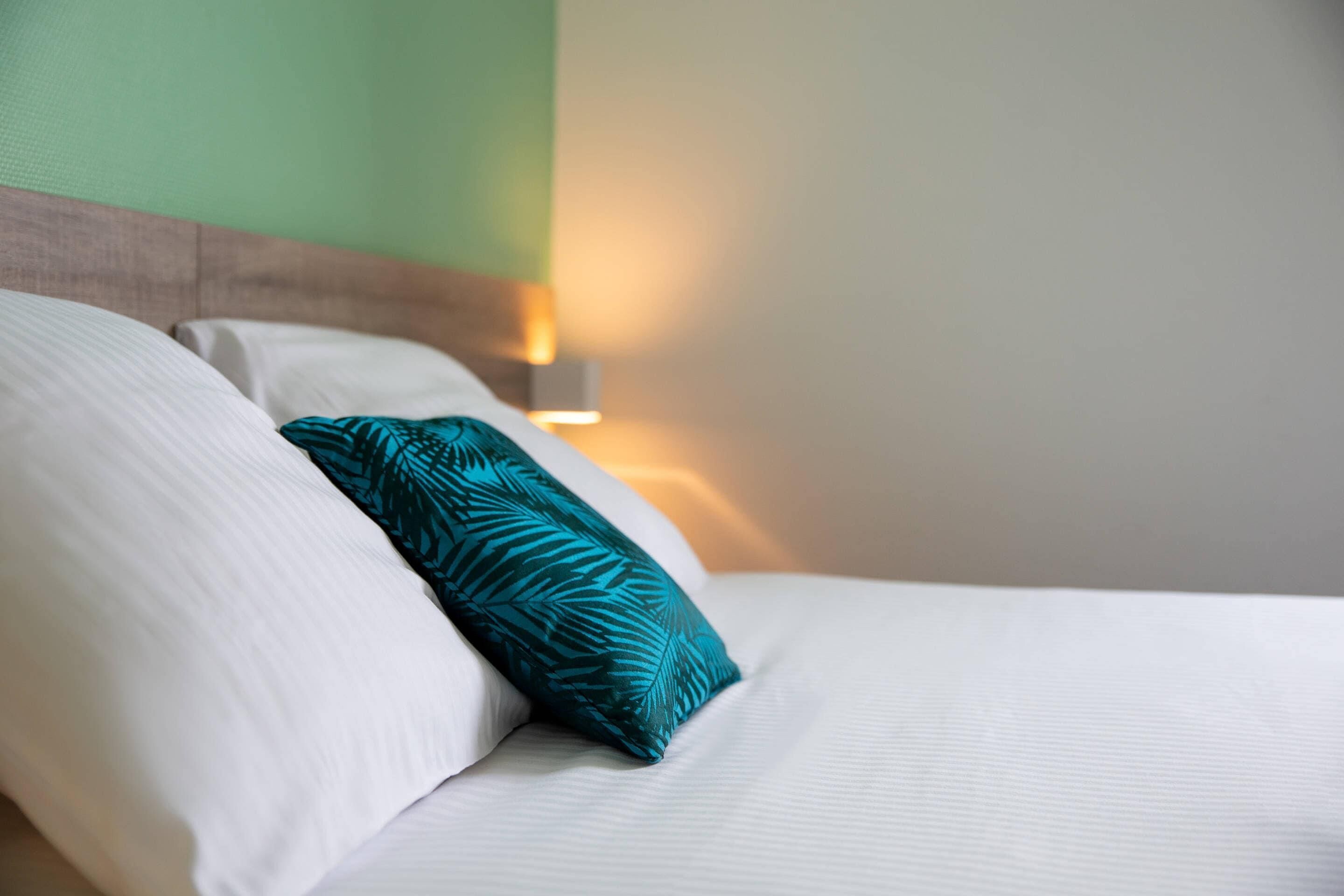 A neatly made bed with white linens and a teal patterned pillow.