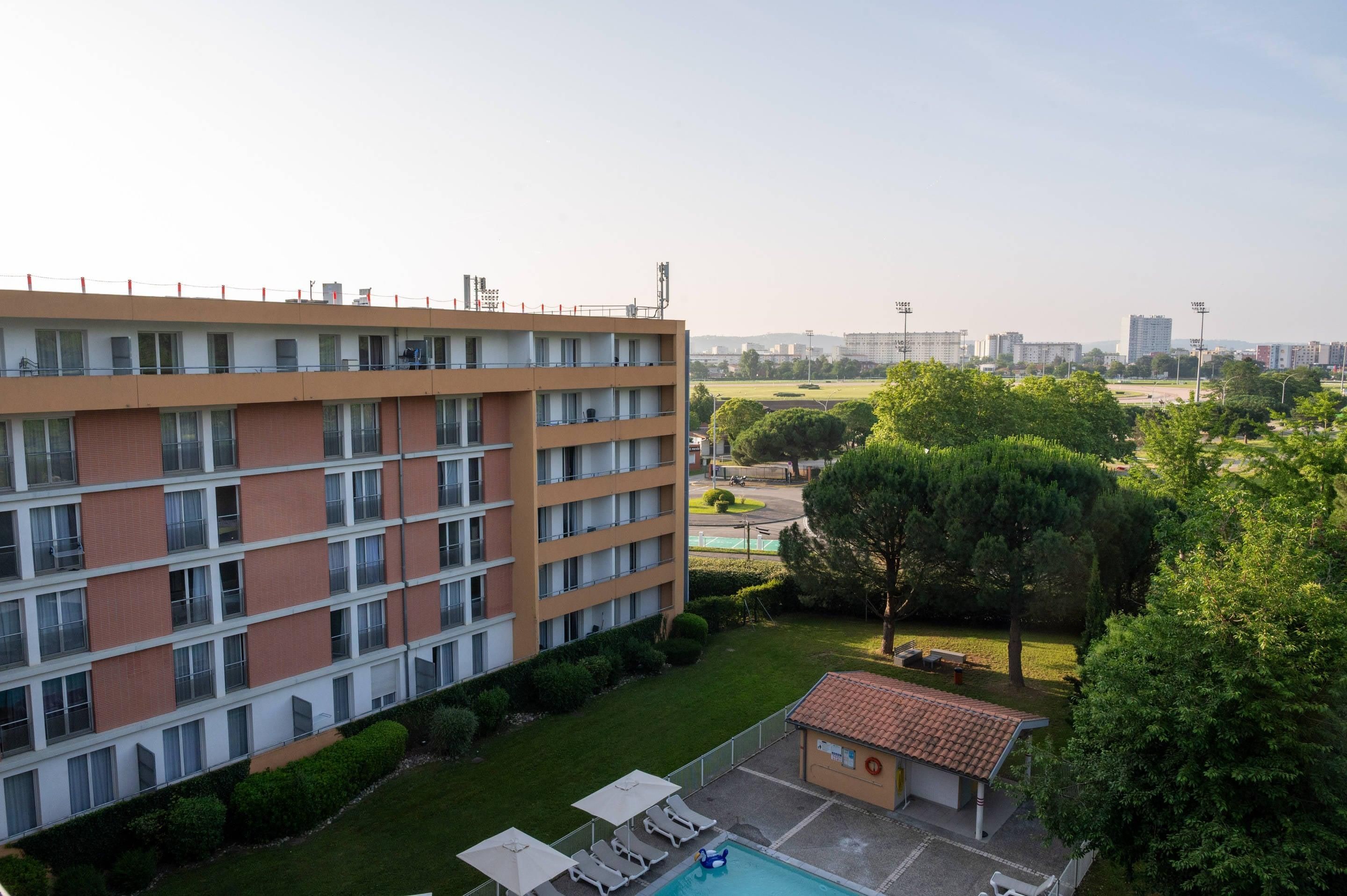 A multi-story hotel with a rooftop terrace, a swimming pool, and a small garden area.