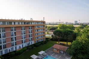 Un hotel de varios pisos con terraza en la azotea, piscina y un pequeño jardín.