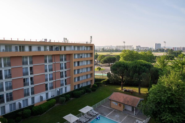 A multi-story hotel with a rooftop terrace, a swimming pool, and a small garden area.