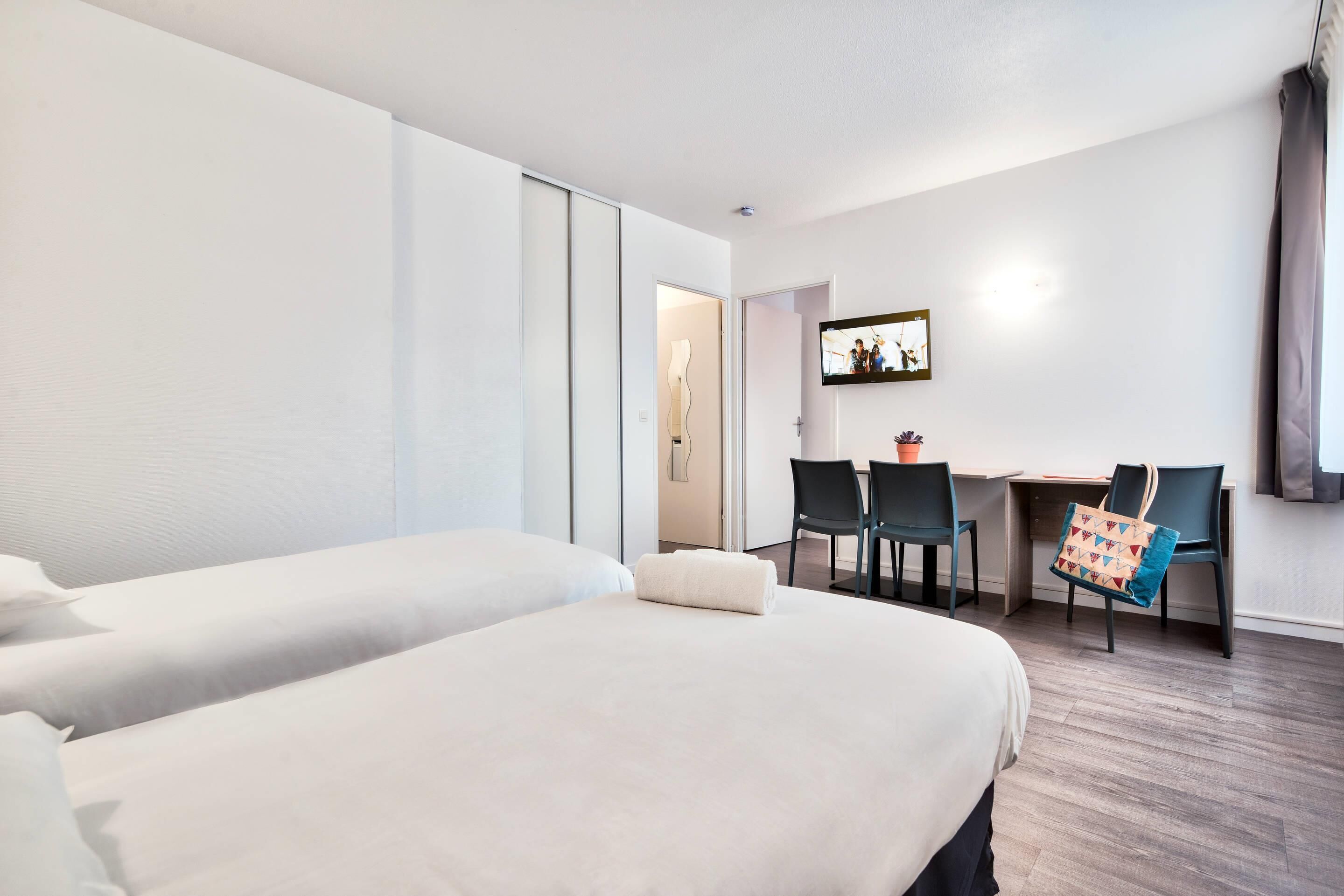 A hotel room with two beds, a desk, and chairs.