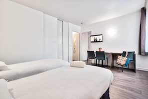 Et hotelværelse med to senge, et skrivebord og stole.