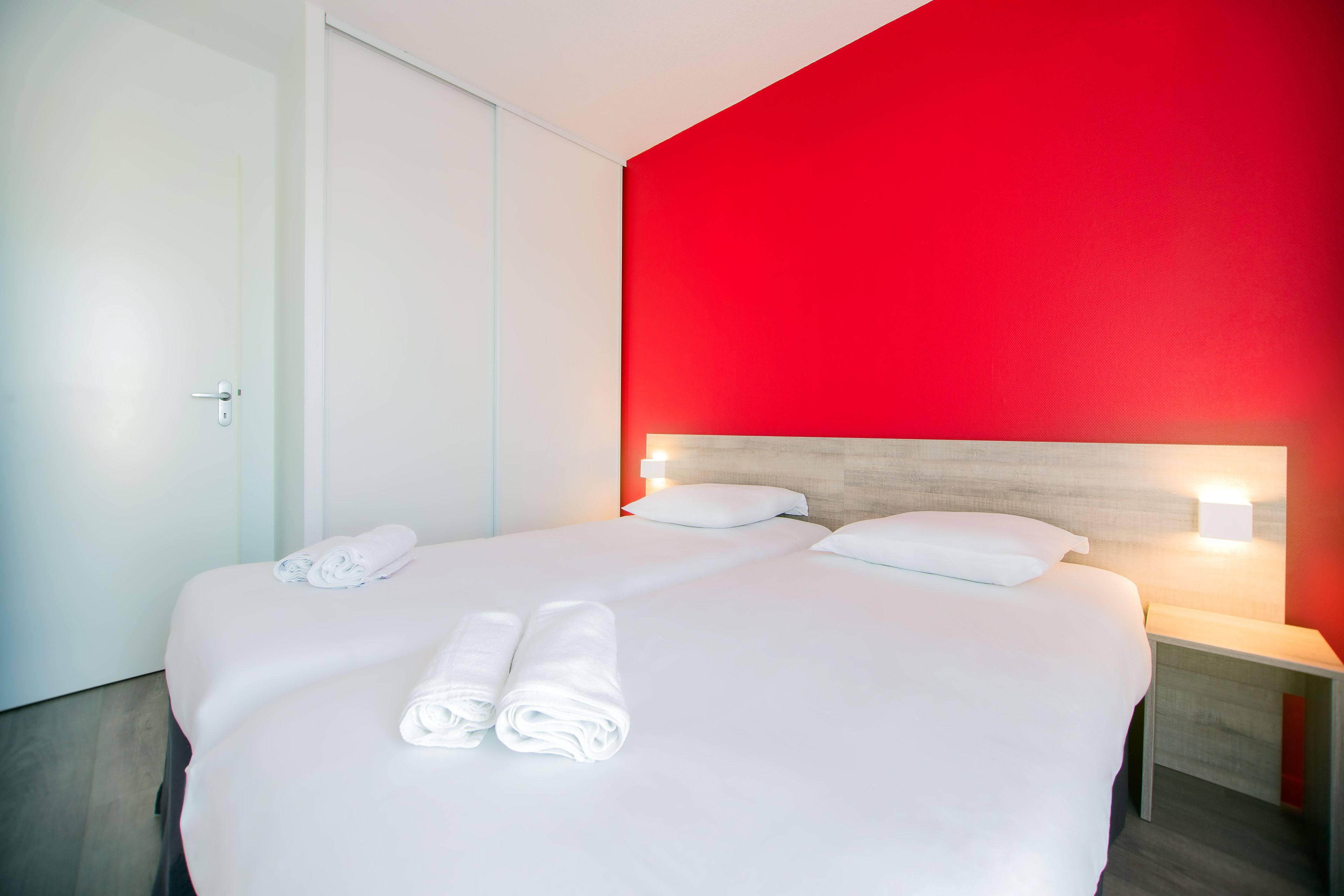 Habitación de hotel con una cama grande, dos mesitas de noche y una pared de acento roja.