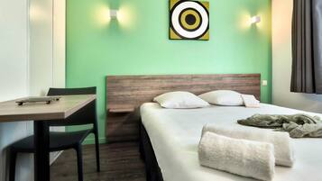 Habitación de hotel con cama, escritorio y silla. Hay un cuadro en la pared y una ventana con cortinas.