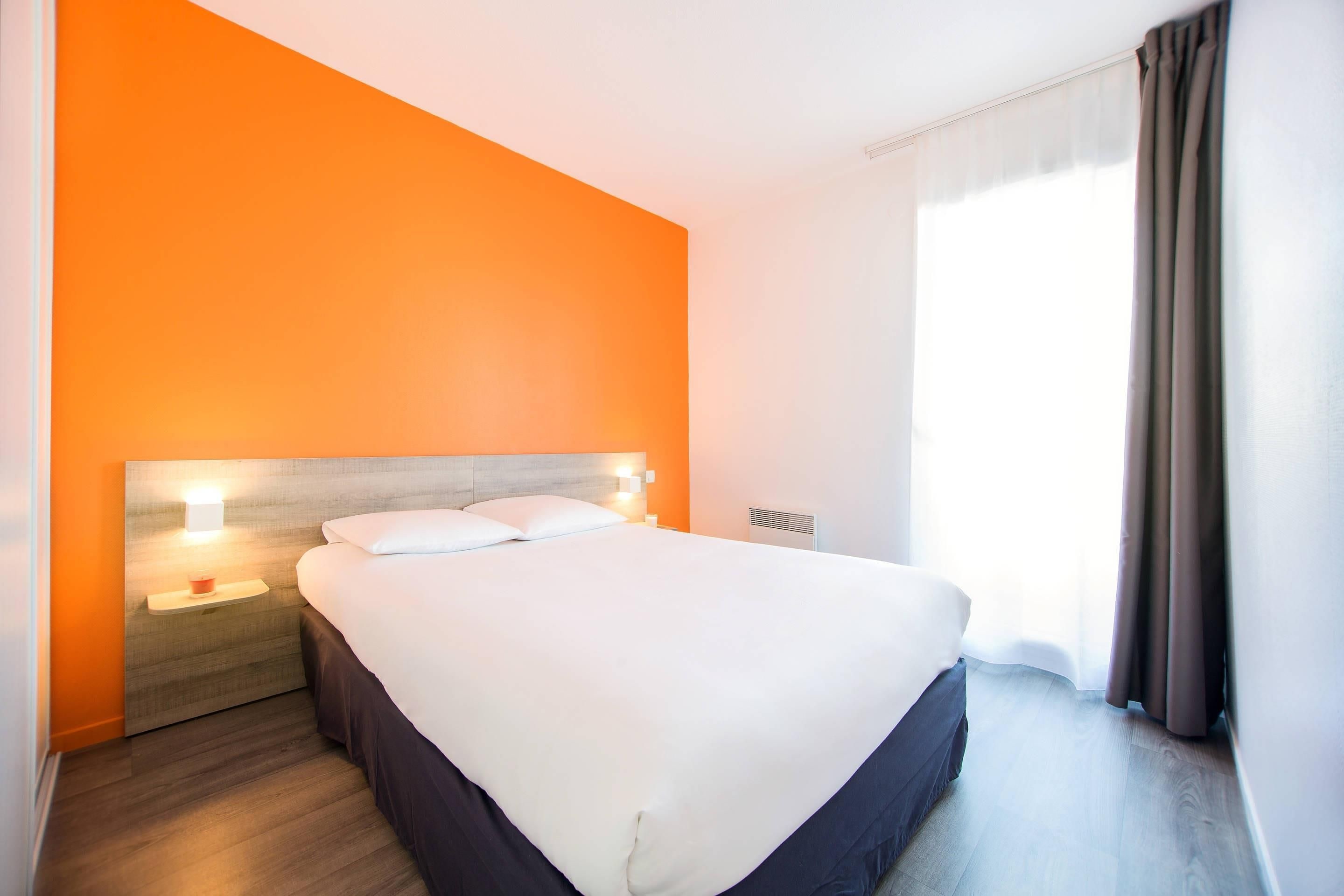 Une chambre d’hôtel avec un grand lit, une table de chevet avec une lampe et une fenêtre avec des rideaux.