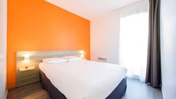 A hotel room with a large bed, a nightstand with a lamp, and a window with curtains.