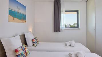 Habitación de hotel con dos camas, una ventana con cortinas, un cuadro de playa y vistas a edificios.