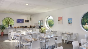 A modern cafe with white furniture, round windows, and artwork on the walls. - Zenitude Hôtel - Résidences Bordeaux Aéroport (Merignac)