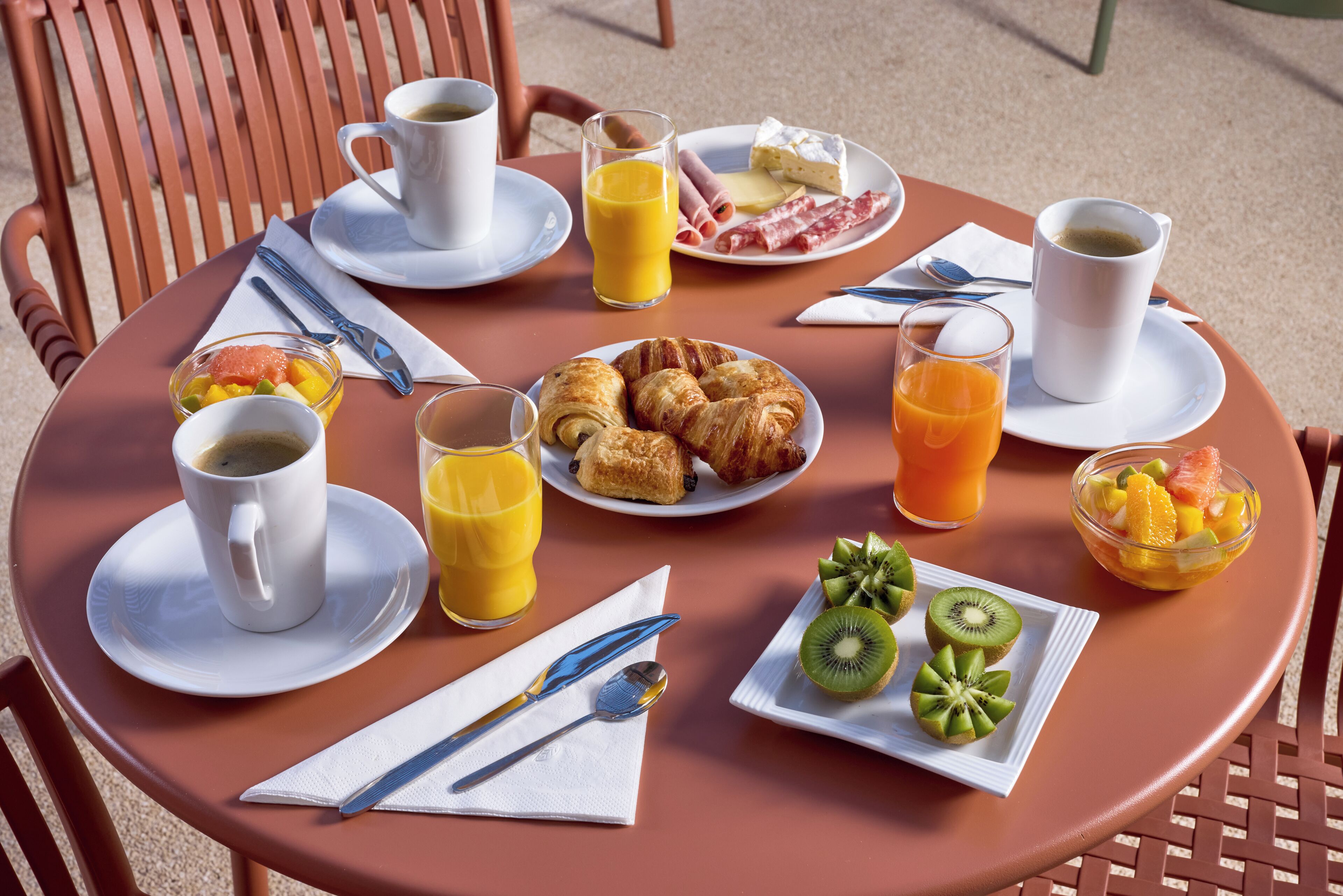 Ein runder Tisch mit Frühstücksangeboten, darunter Croissants, Obst und Getränke.