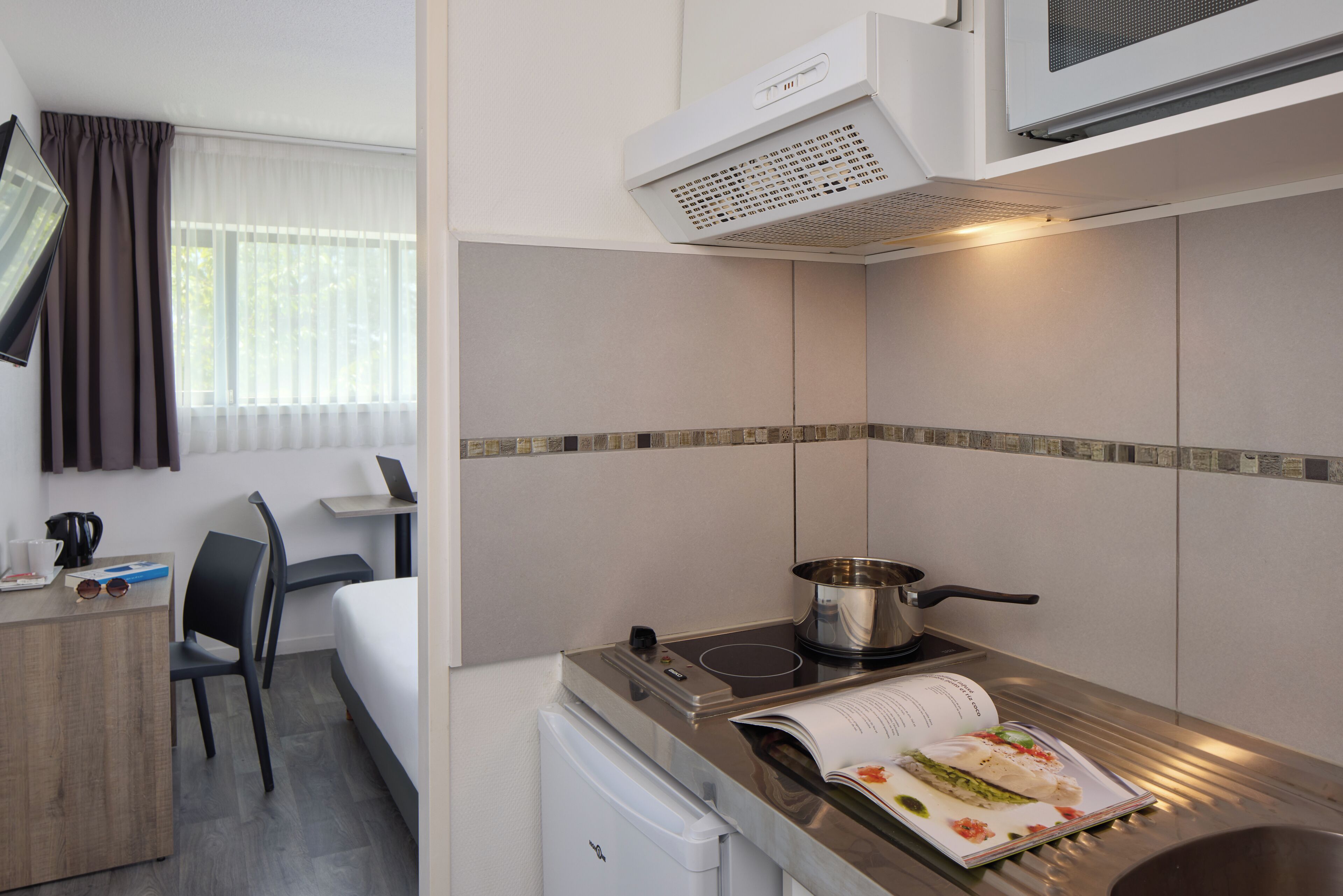 A compact hotel room with a kitchenette, a small dining area, and a bed.
