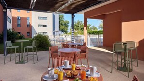 An outdoor patio with tables and chairs, breakfast items, and a view of buildings in the background. - Zenitude Hôtel - Résidences Bordeaux Aéroport (Merignac)