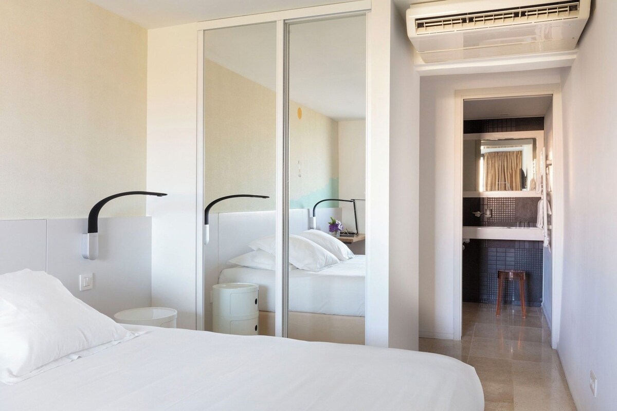 Ein Hotelzimmer mit Bett, Nachttisch, Spiegel und einem durchgegangenen Tür erkennbaren Badezimmer.