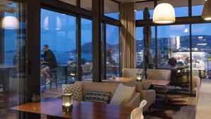 A modern hotel room with large windows, a cozy seating area, and a view of the cityscape. - Hotel Alcyon Porto Vecchio (Porto-Vecchio)
