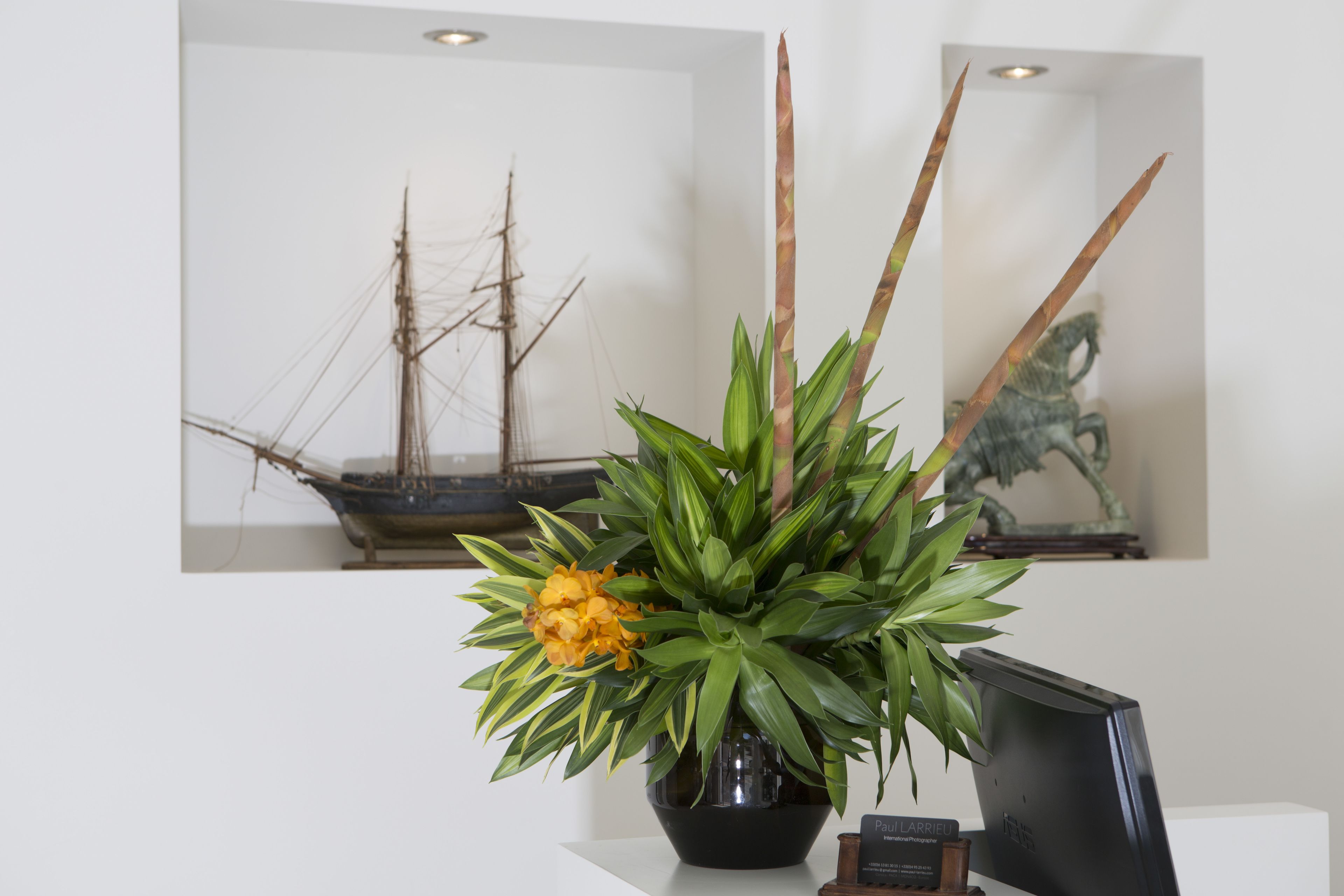 A desk with a potted plant, a framed picture of a ship, and a computer monitor.
