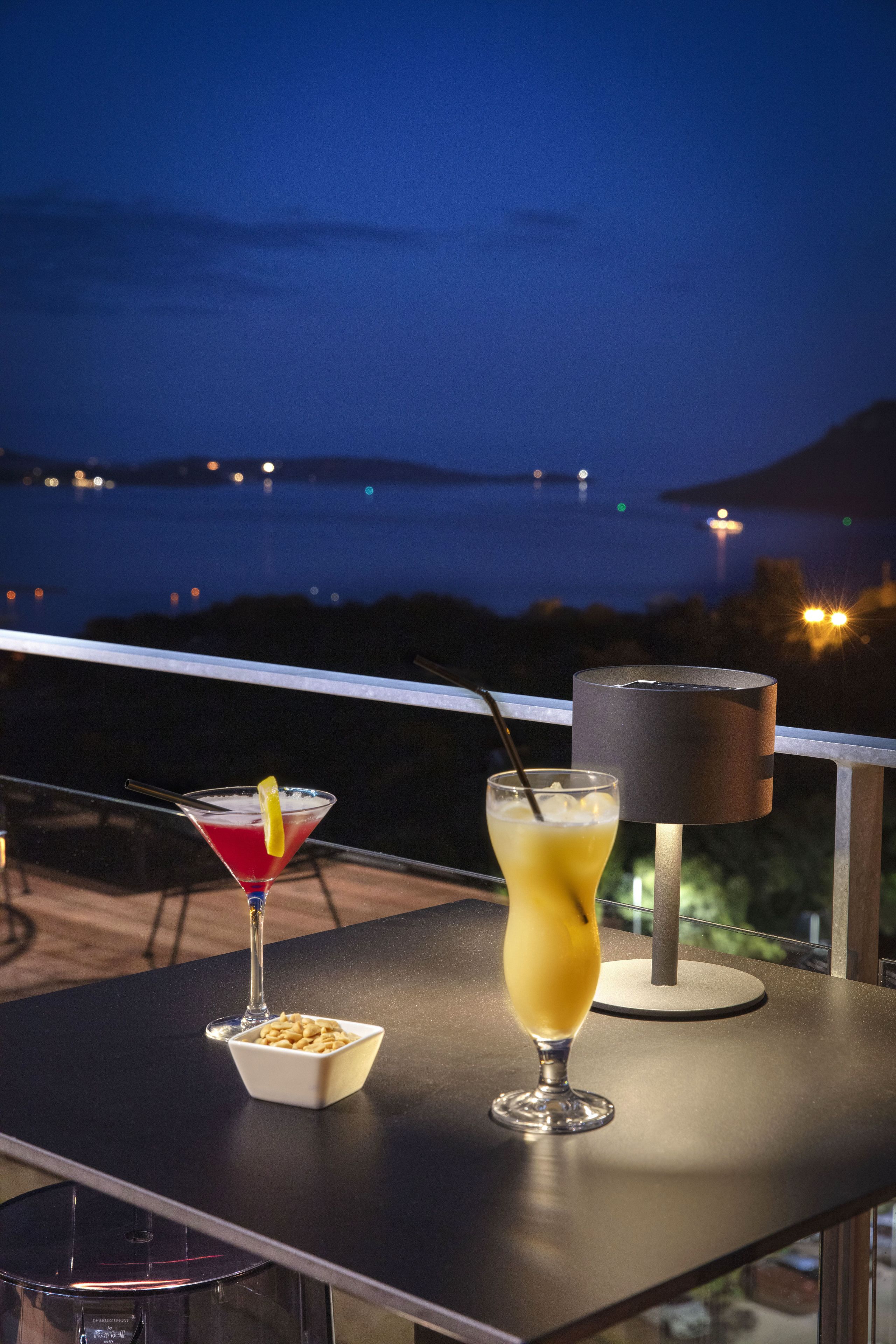 A balcony with two drinks, a bowl of nuts, and a lamp.