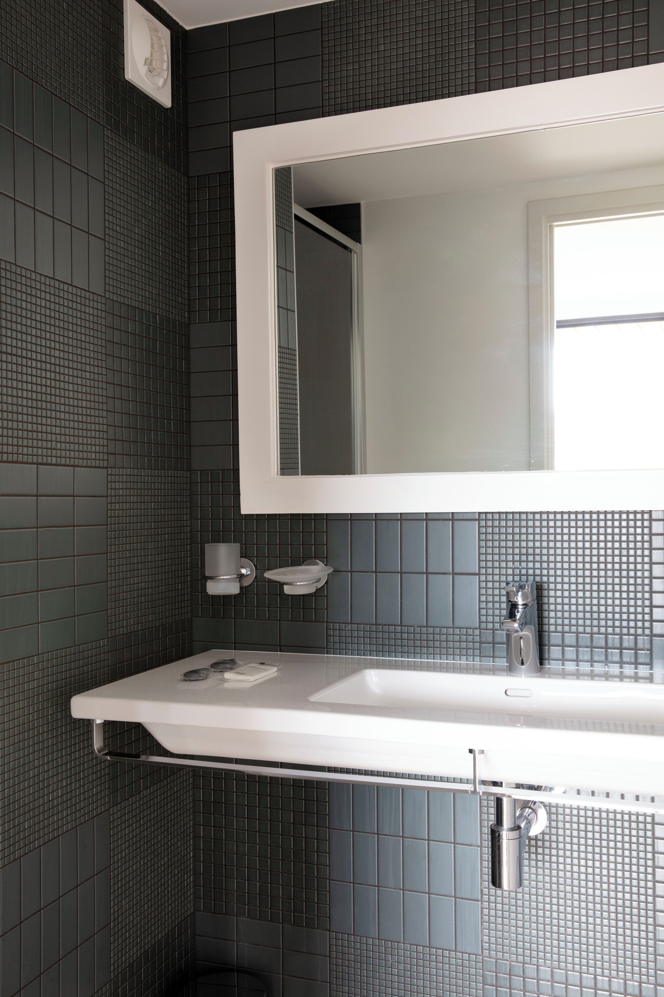 A bathroom with a white sink, a mirror, and a tiled wall.
