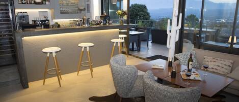 A modern bar area with stools, a dining table with chairs, and a view of the mountains through large windows.