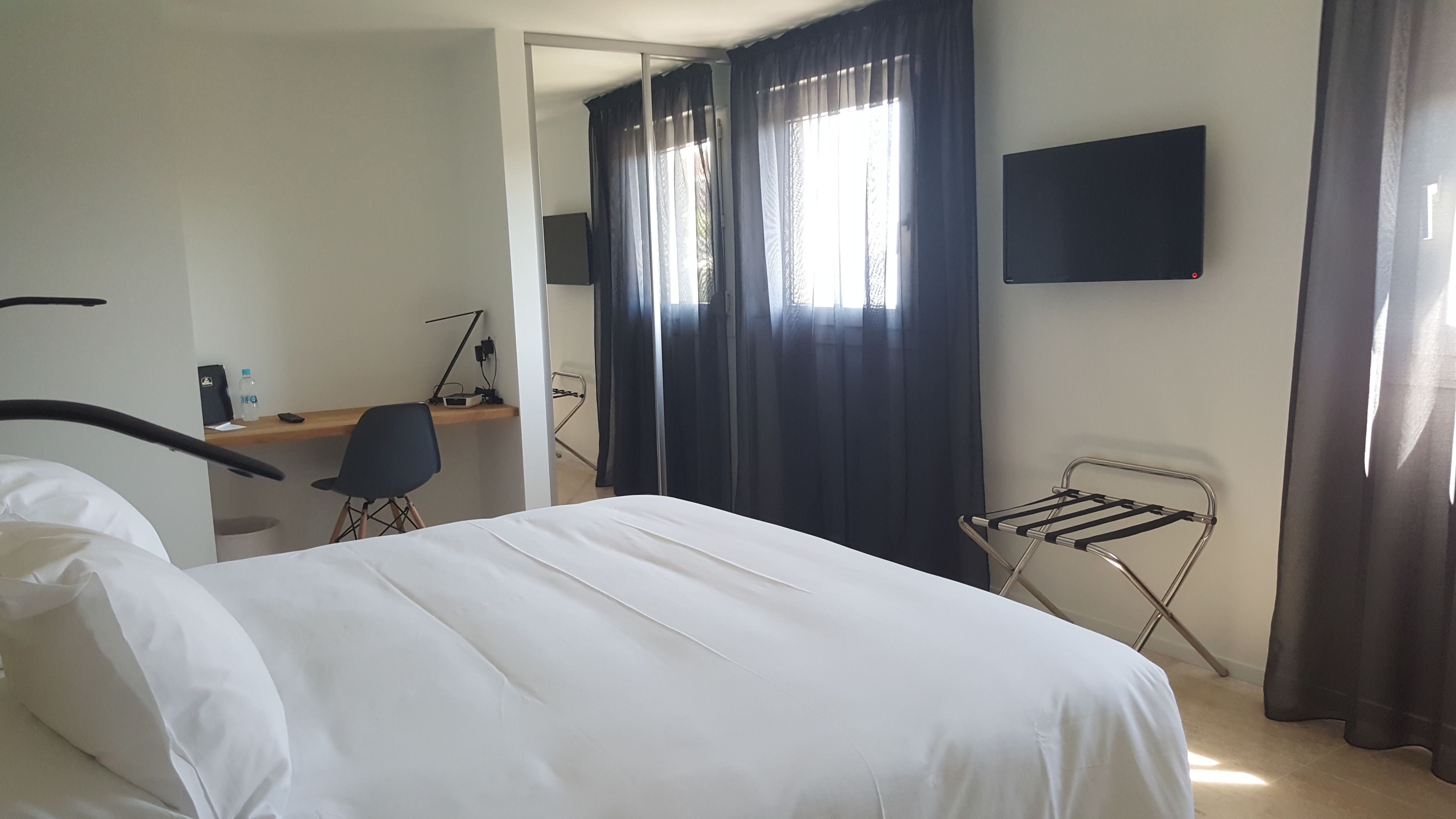 Habitació d'hotel amb un llit, una taula de treball amb una cadira, un televisor fixat a la paret i una finestra amb cortines.