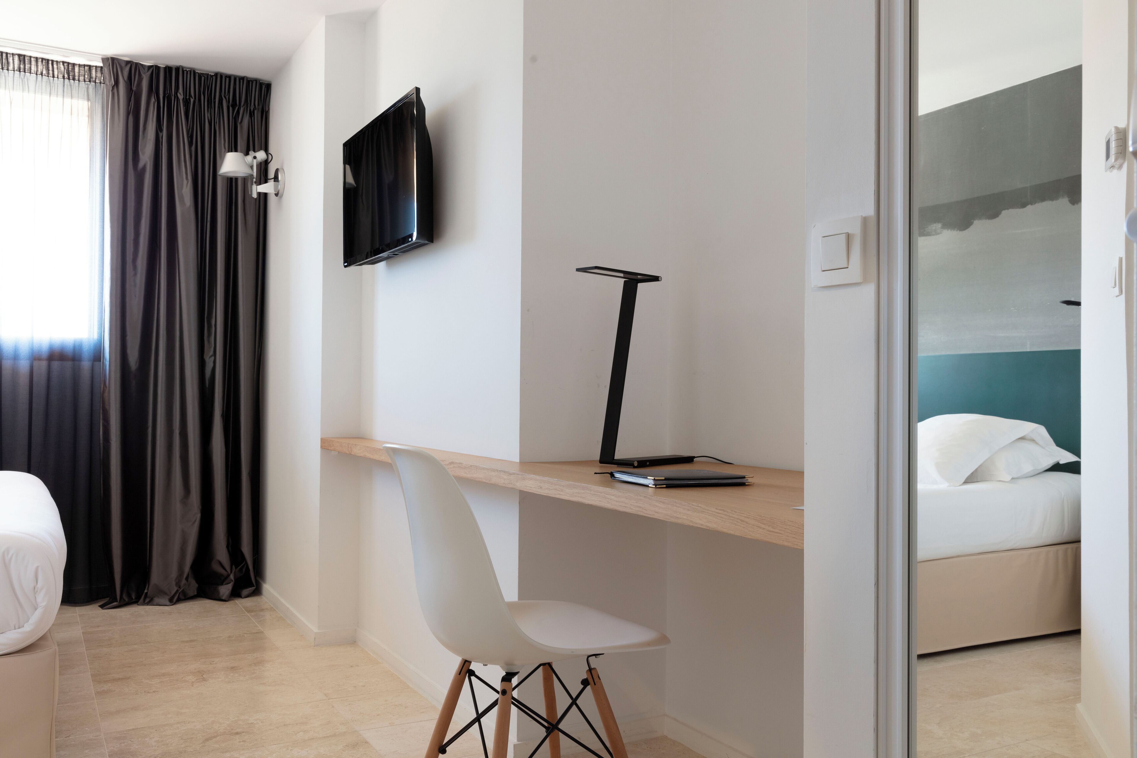 Et moderne hotelværelse med seng, skrivebord med stol, fjernsyn ophængt på væggen og havudsigt fra et vindue.