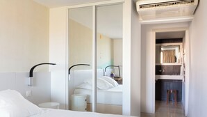 A hotel room with a bed, a mirror, a small table, a nightstand, a wall-mounted air conditioner, and a bathroom visible through an open door. - Hotel Alcyon Porto Vecchio (Porto-Vecchio)