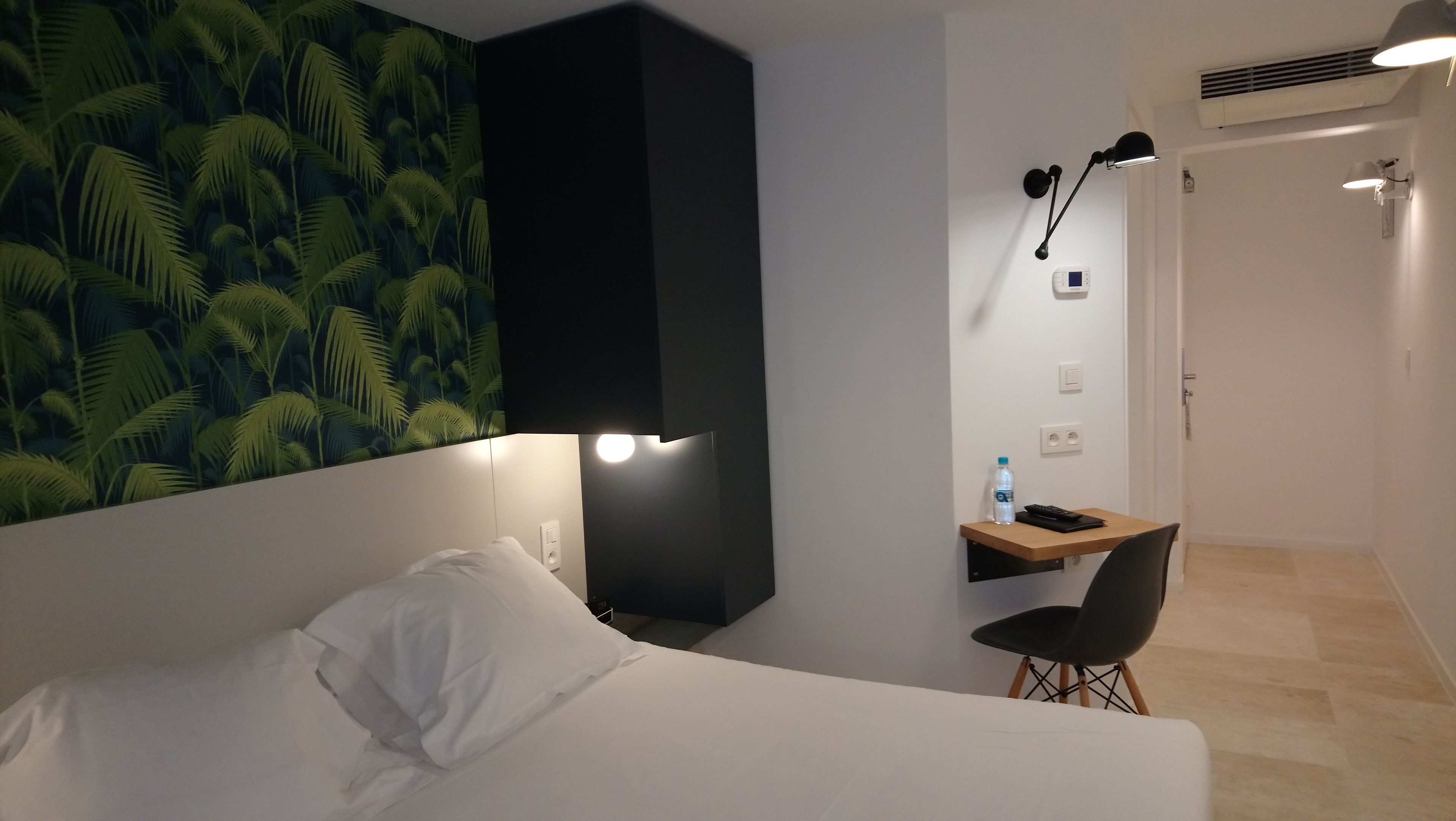 Een hotelkamer met een bed, een bureau met stoel, een waterfles en een afstandsbediening.