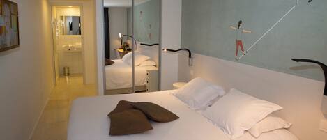 Quarto de hotel com cama, banheiro com espelho e parede com quadro.