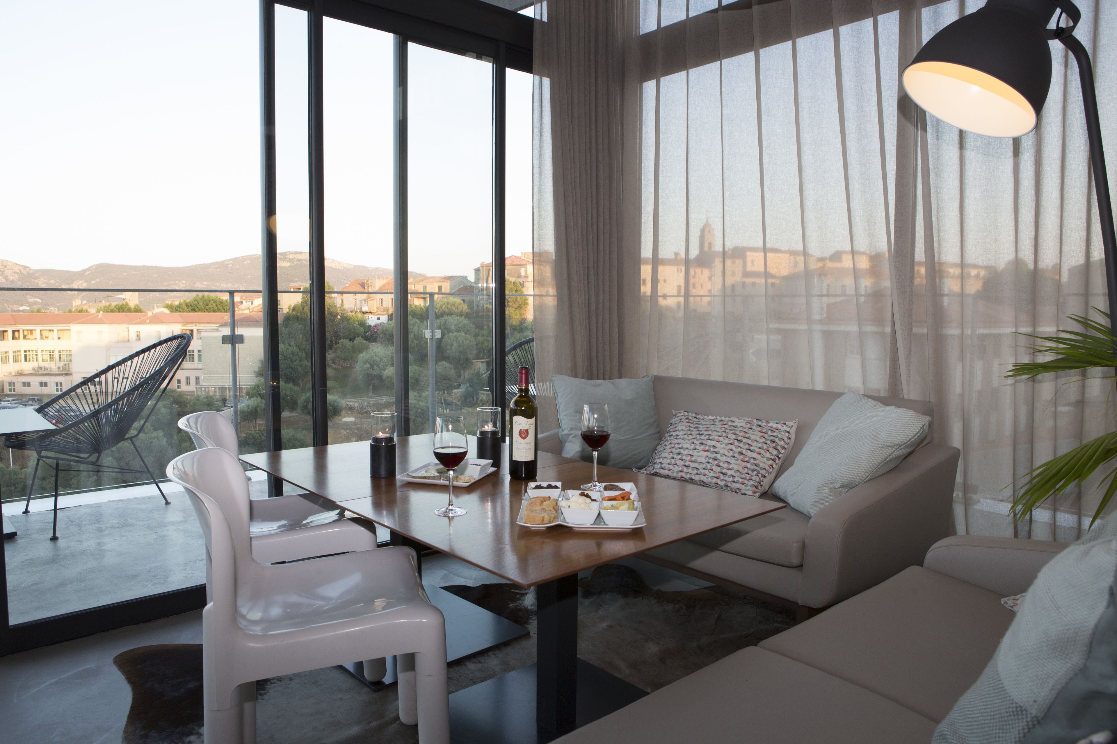 A modern living room with a sofa, a dining table with chairs, and a balcony with a view of the city.
