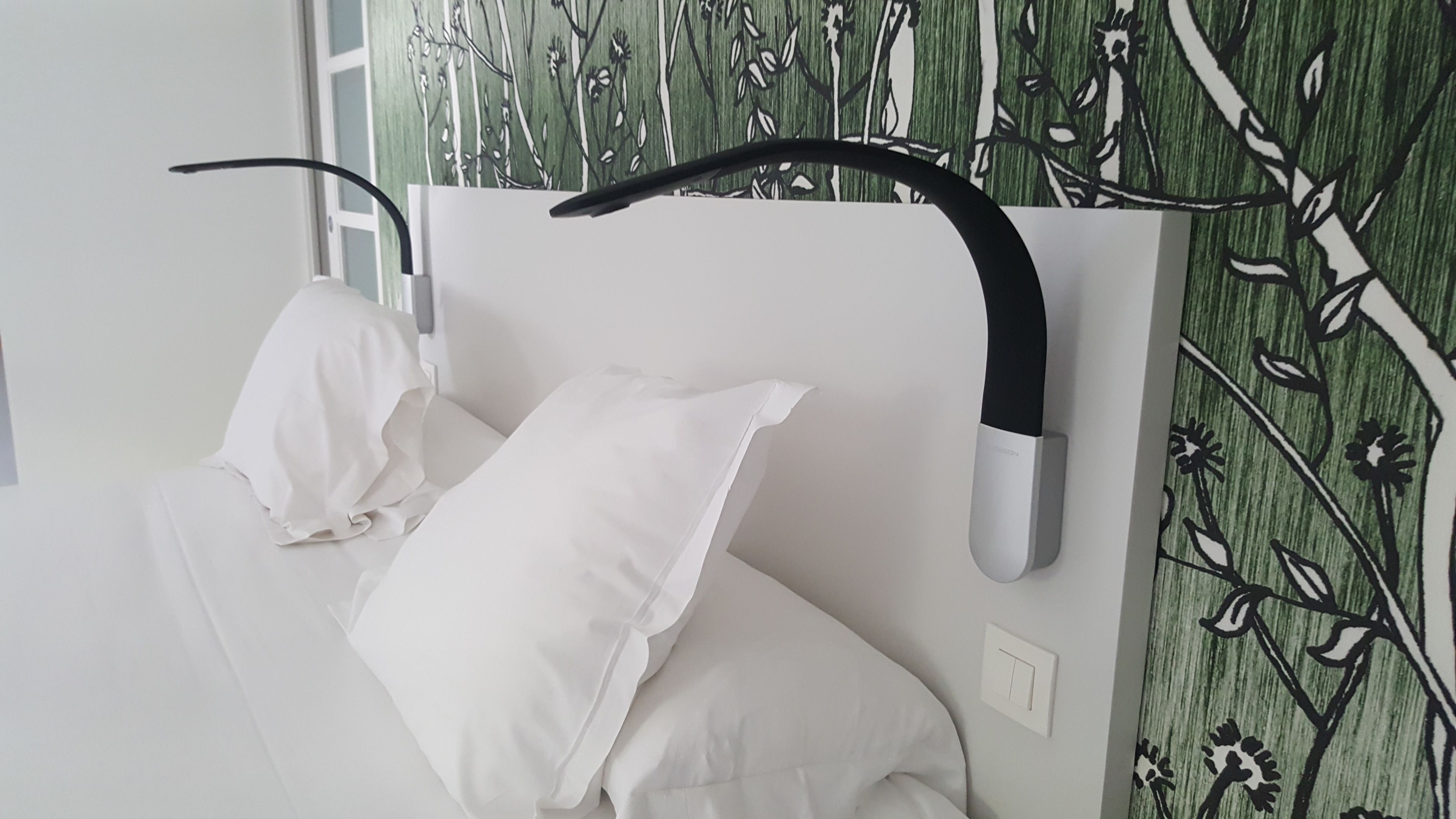 Un dormitorio moderno con cama blanca, cabecero negro curvo y papel tapiz floral verde.