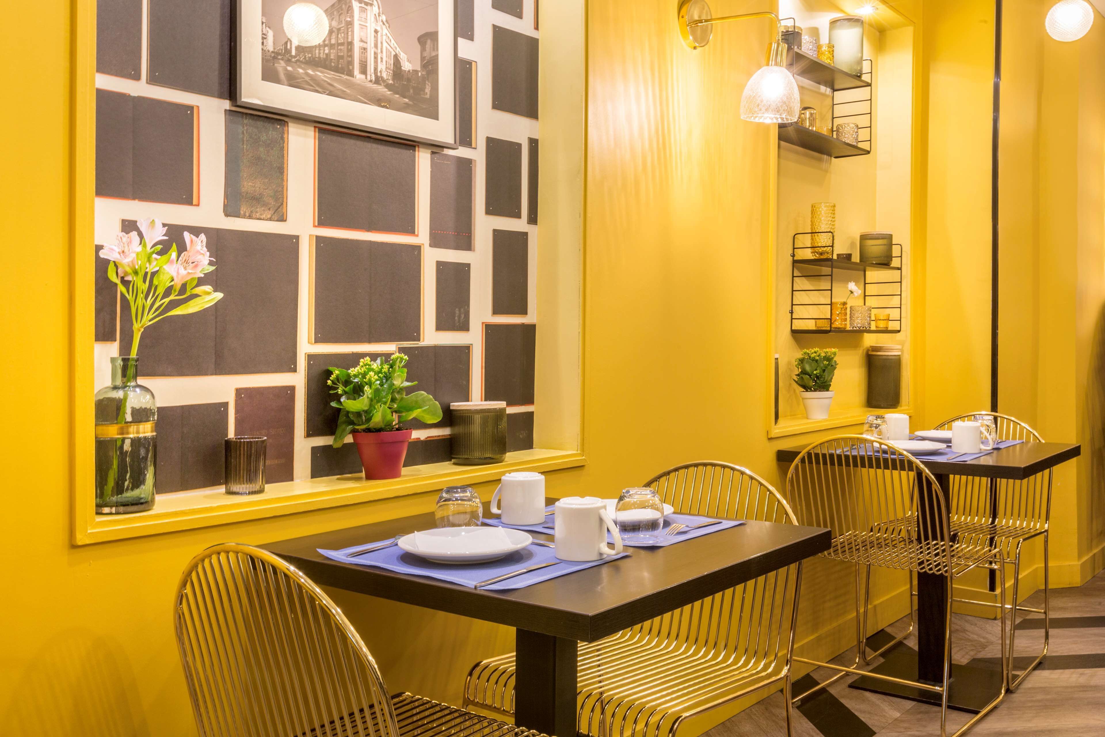 A dining area with a table set for four, chairs, a vase with flowers, and a wall with framed pictures.