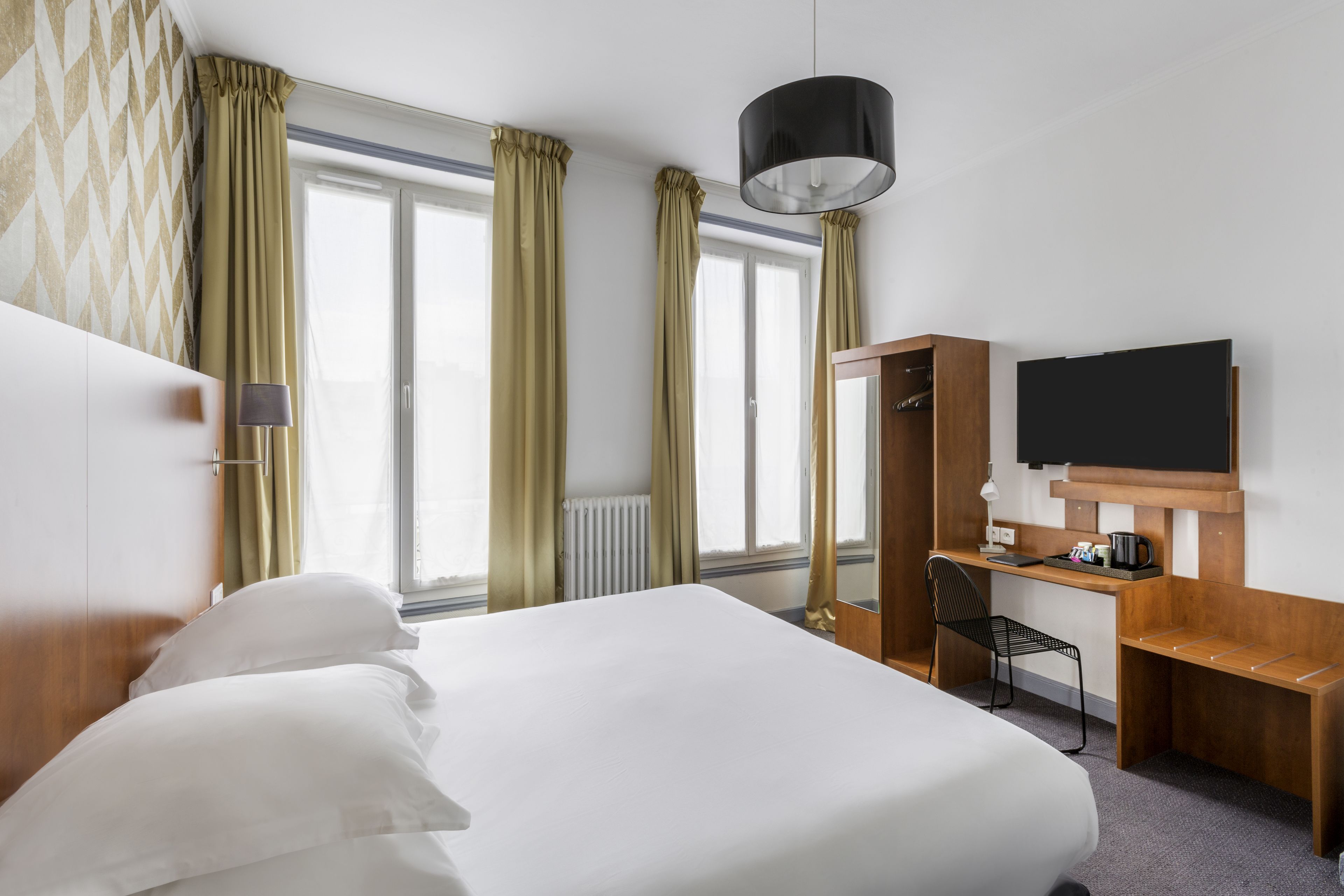 Una habitación de hotel con una cama grande, un escritorio con una silla, un televisor y una ventana con cortinas.