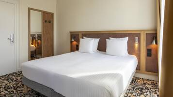 Une chambre d’hôtel avec un grand lit, une tête de lit en bois, deux lampes fixées au mur et un sol à motifs.
