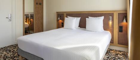 Habitación de hotel con una cama grande, cabecera de madera, dos lámparas de pared y suelo estampado.